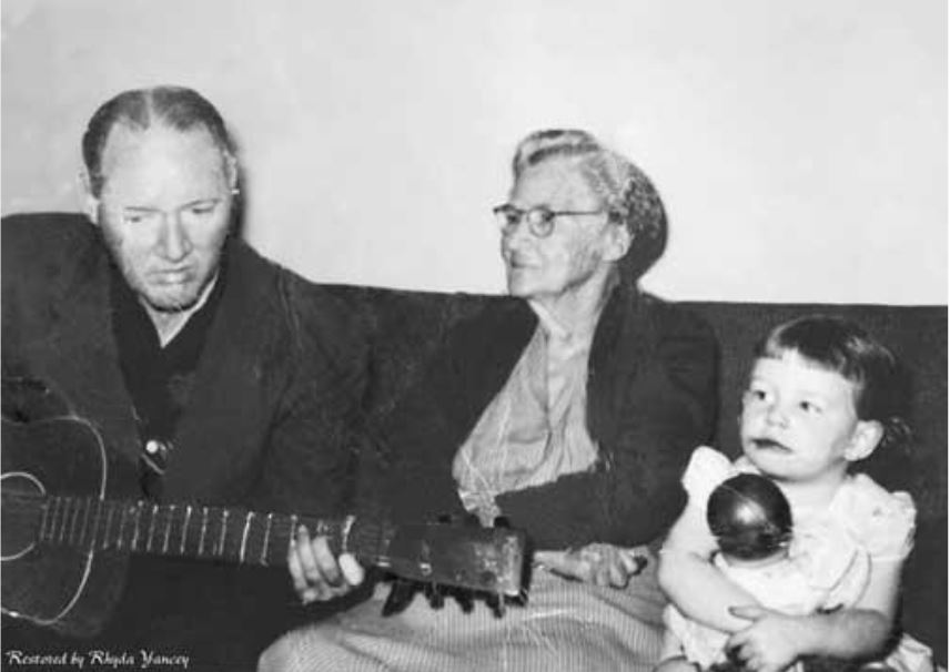 Man playing guitar with an elderly woman and a young girl holding a maraca, capturing a family moment of music and joy.